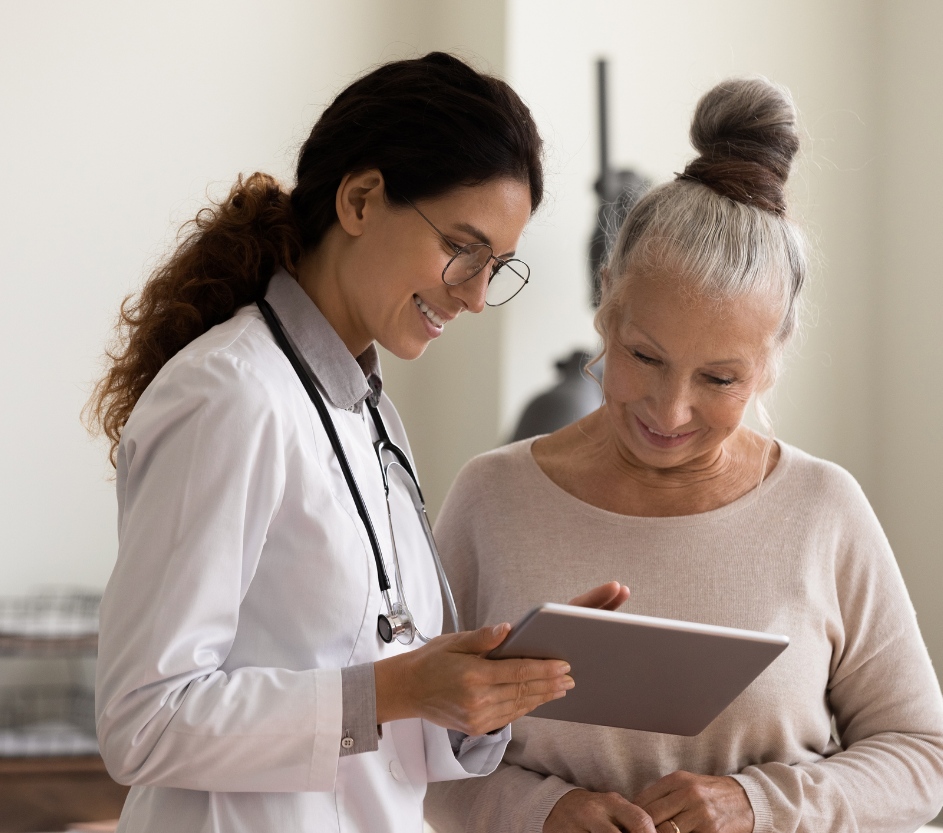 Hay una doctora al lado de una mujer, las dos juntas están mirando una tablet.