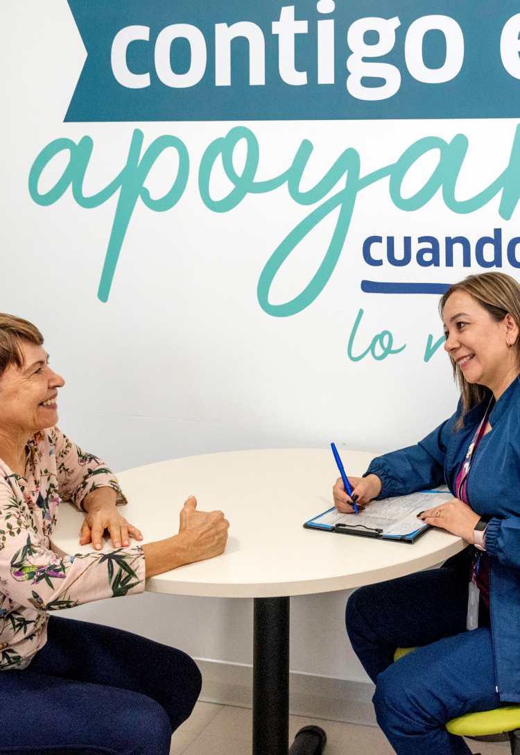 Profesional de la salud sentada en un escritorio, diligenciando a mano una planilla, con los datos que le proporciona la paciente que tiene enfrente.